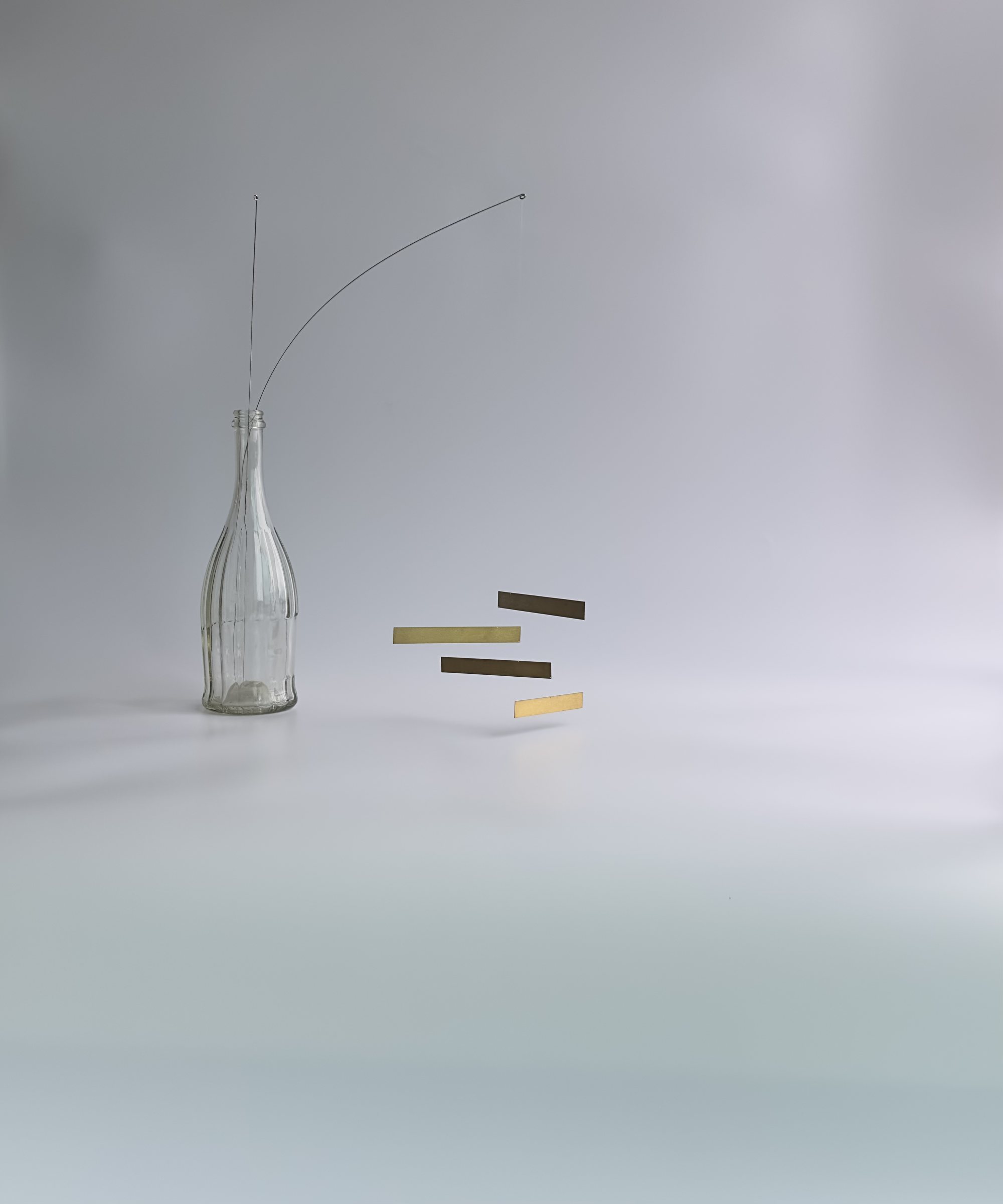MOBILE 01 — four metal pieces hanging from a wire set in a glass bottle